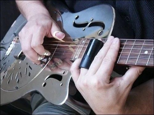 Nahaufnahme einer Resonatorgitarre mit Metall-Slide am Griffbrett