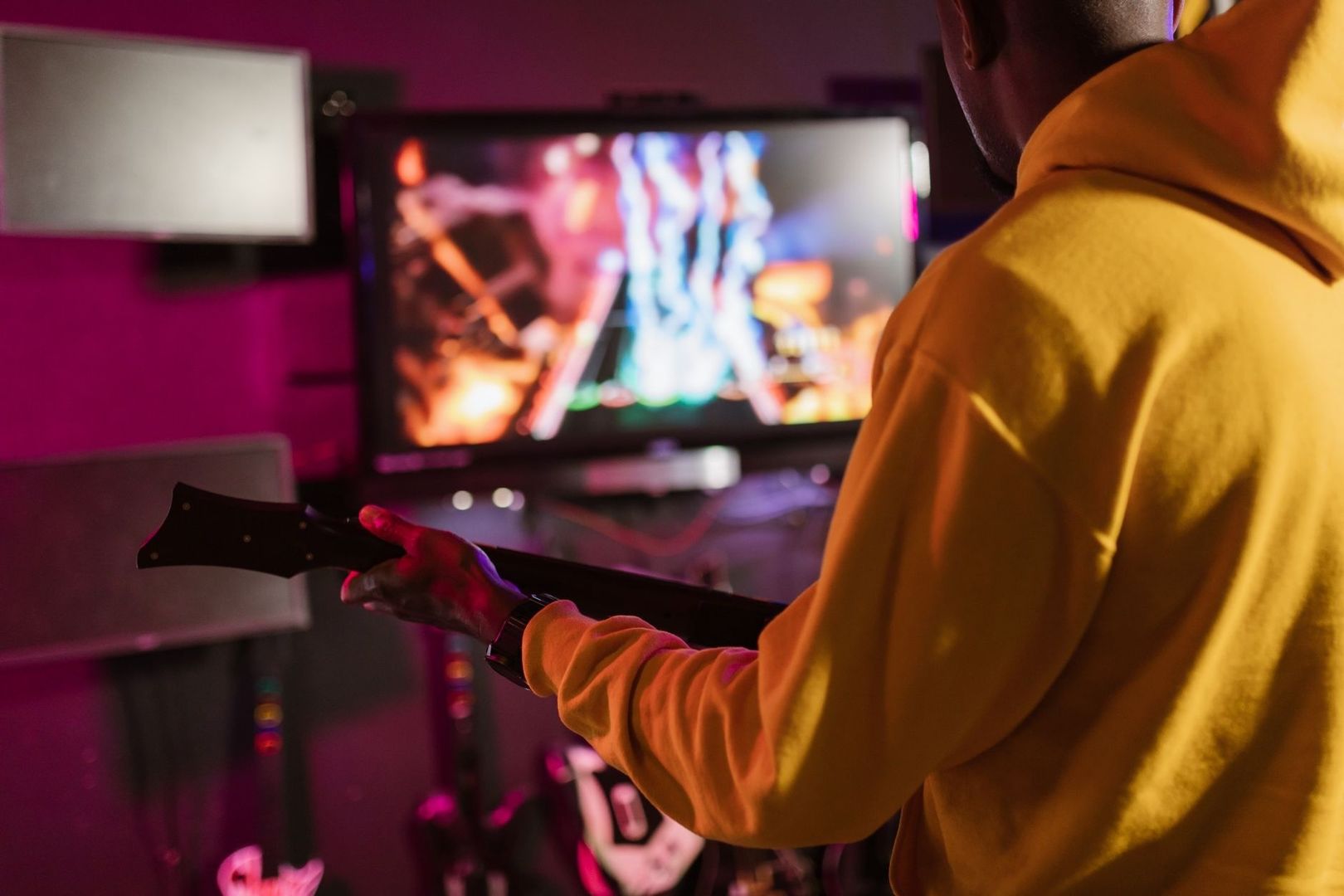 Person mit Gitarre vor einem Bildschirm mit farbenfrohem Musikspiel